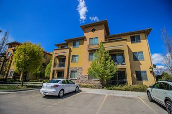 A silver car is parked in a parking lot in front of a tan apartment building.